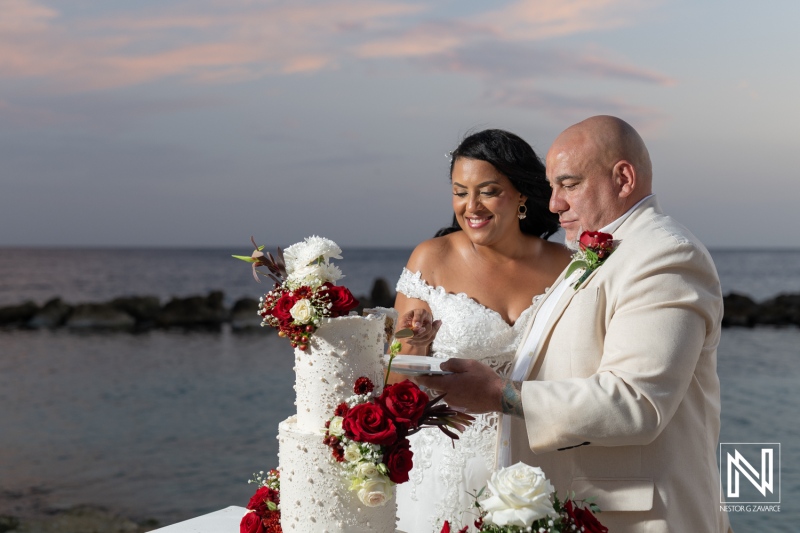 Couple celebrates their wedding at Sunscape Curacao Resort with a beautifully decorated cake against a stunning ocean backdrop during sunset
