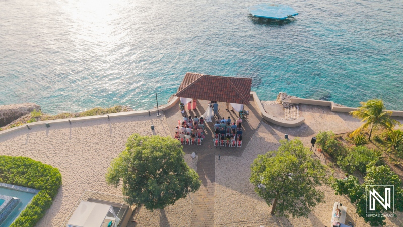 Wedding ceremony taking place by the water at Dreams Curacao Resort Spa Casino in Curacao with guests seated in attendance