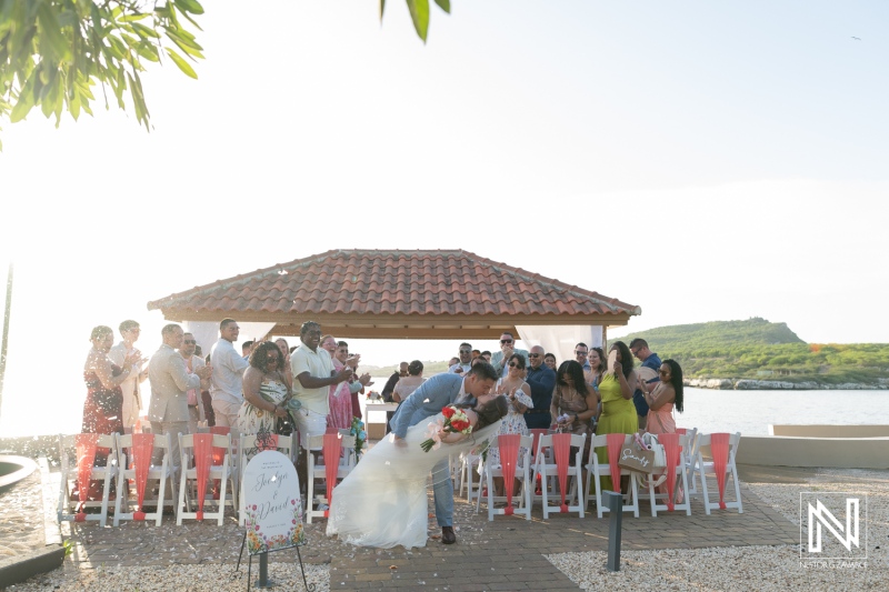 Couple exchanges vows during a wedding ceremony at Dreams Curacao Resort in the evening light with friends and family in attendance