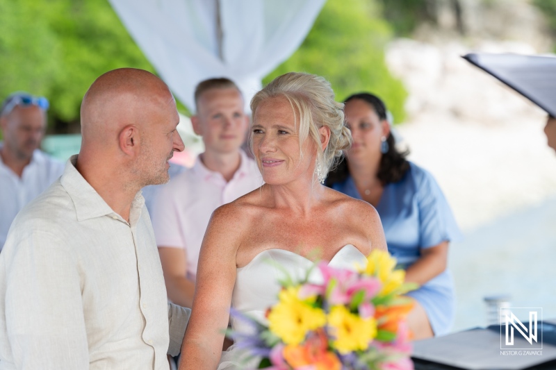 Couple exchanges vows during a romantic wedding ceremony in Curacao with tropical backdrop and vibrant floral arrangements