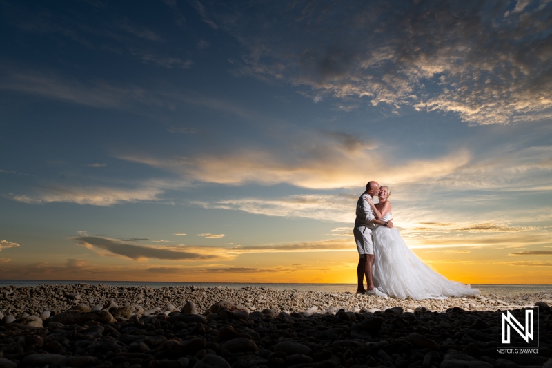 Beautiful wedding couple embraces on Curacao beach at sunset, creating a romantic atmosphere with vibrant skies in the background