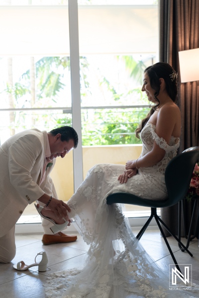 Groom assisting bride with wedding shoes at Avila Beach Hotel in Curacao amidst lush tropical scenery