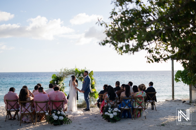 Beautiful wedding ceremony at Playa Hunku in Curacao with a scenic view of the ocean and guests witnessing the vows exchanged