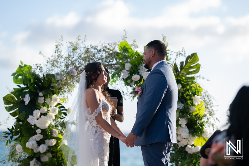 Beautiful wedding ceremony at Playa Hunku in Curacao with stunning floral arch and ocean backdrop during golden hour