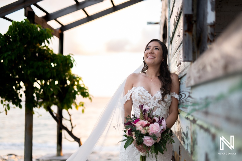 Bride in a beautiful wedding dress smiles while holding a bouquet at Playa Hunku in Curacao during sunset