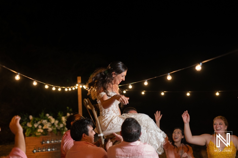 Joyful celebration at a Curacao wedding in Playa Hunku featuring the bride being lifted in a traditional chair dance surrounded by happy guests