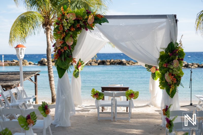 Romantic Beach Wedding Setup Featuring a Beautifully Decorated Arch With Tropical Flowers and Seating Under Palm Trees Beside the Ocean