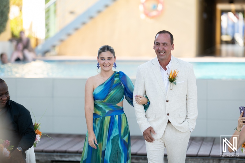 A Joyful Couple Walks Down the Aisle at a Tropical Wedding Ceremony Beside a Shimmering Pool in a Vibrant Outdoor Setting Under Bright, Clear Weather