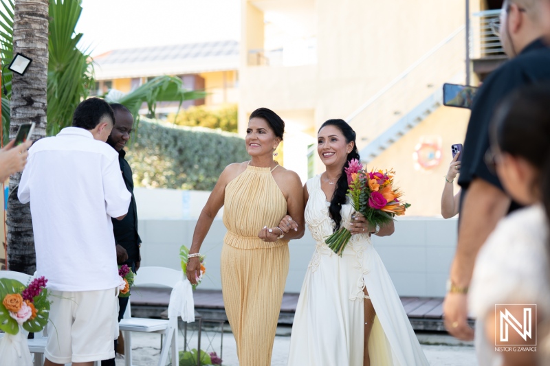 Bride and Mother Walking Down the Aisle at a Tropical Beach Wedding Ceremony, Surrounded by Guests Enjoying the Sunny Atmosphere