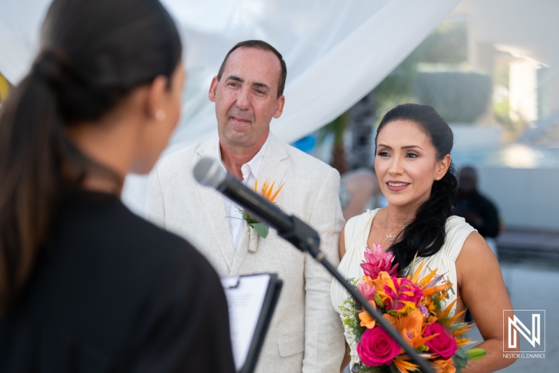 A Couple Exchanges Vows During a Tropical Wedding Ceremony Under a Beautifully Draped Backdrop, Surrounded by Vibrant Flowers and Warm Sunlight in a Serene Location