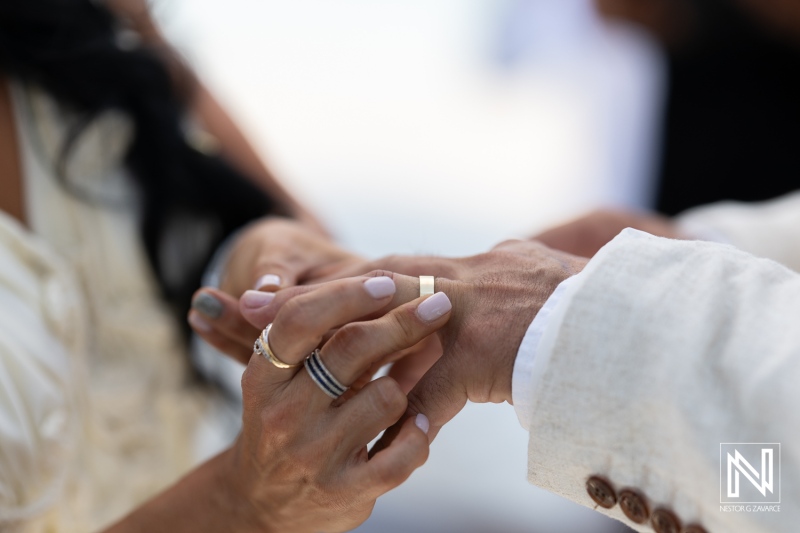 A Couple Exchanging Wedding Rings During Their Ceremony by the Ocean on a Sunny Day, Celebrating Their Commitment to Each Other in a Romantic Setting