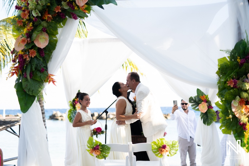 Couple Exchanging Vows During Their Tropical Beach Wedding Ceremony at Sunset With Floral Decorations and Joyful Guests Nearby