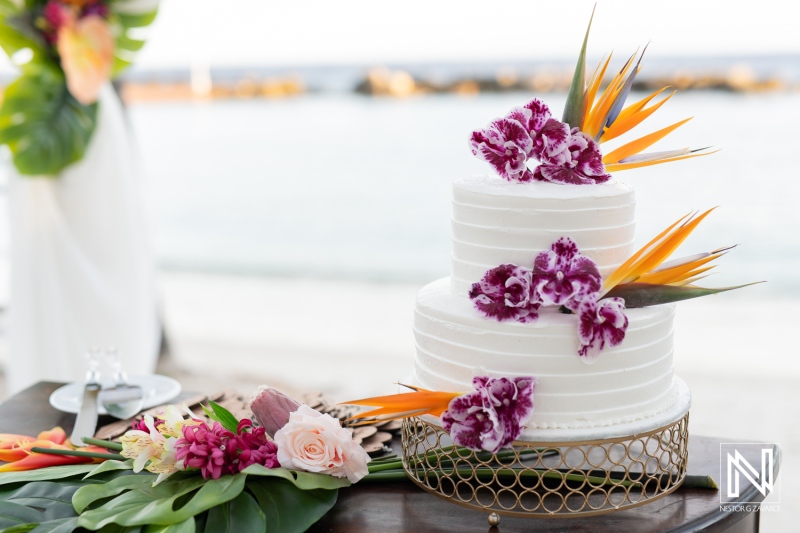 A Beautifully Decorated Wedding Cake Adorned With Orchids and Tropical Flowers on a Table by the Waterfront During a Sunny Day Celebration