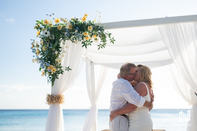 Couple shares a romantic kiss during their wedding ceremony at Playa Porto Mari in Curacao under a floral arch