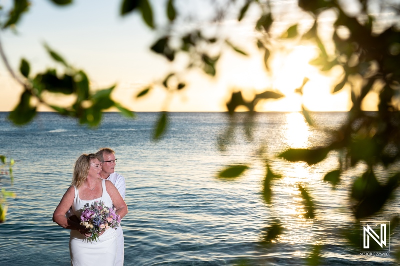 Romantic wedding ceremony at Playa Porto Mari in Curacao during a vibrant sunset with a happy couple embracing by the water