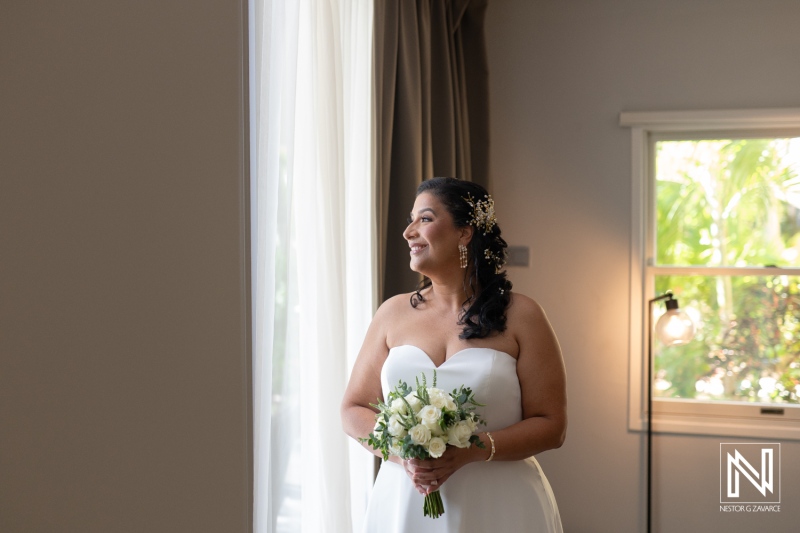 Bride holding bouquet and gazing out the window in a Curacao wedding venue filled with natural light