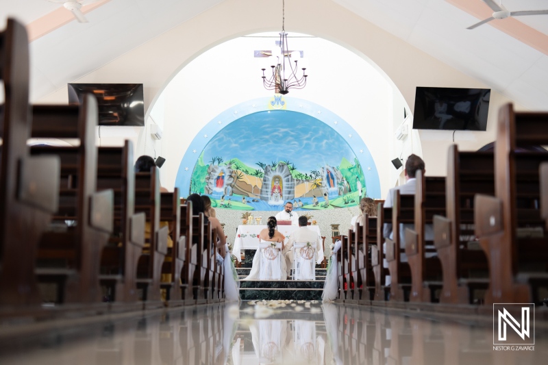 Wedding ceremony takes place indoors in a beautifully decorated church in Curacao with an elegant backdrop and gathered guests witnessing the vows being exchanged