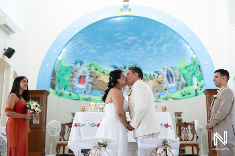 Couple shares a kiss during their wedding ceremony in Curacao, surrounded by loved ones and vibrant decor