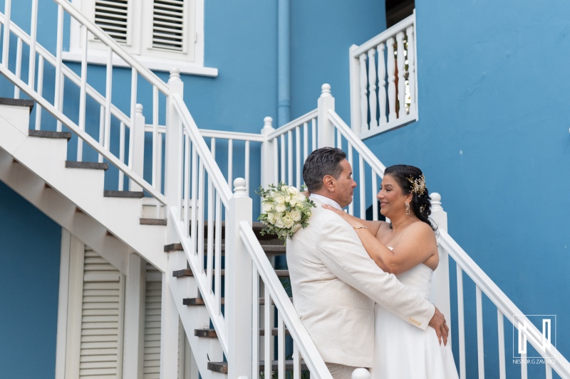 Couple embraces on the stairs of a charming blue building in Curacao during a romantic wedding ceremony at sunset