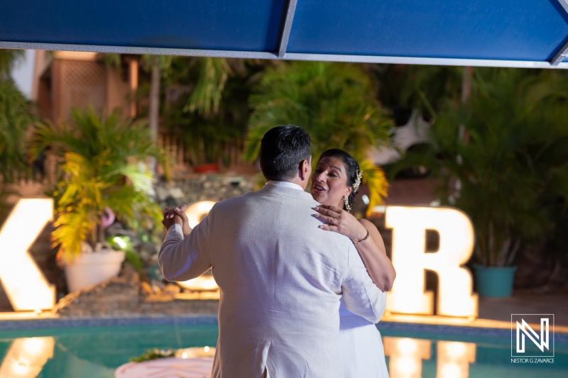 Couple dances joyfully at their wedding celebration in Curacao under a glowing canopy beside a serene pool