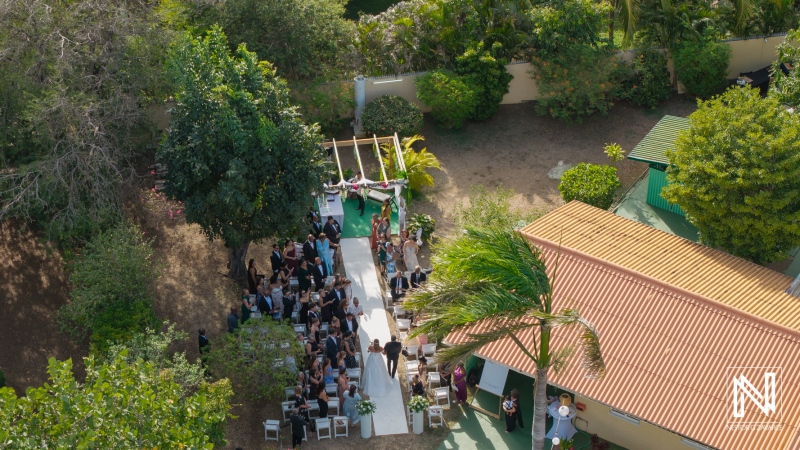 Wedding ceremony taking place in a lush outdoor setting in Curacao, with guests seated and a decorated aisle leading to the altar in a tropical atmosphere
