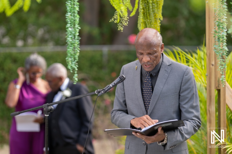 Ceremony officiant reads vows during a beautiful wedding celebration in Curacao, featuring lush greenery and joyous guests in the background