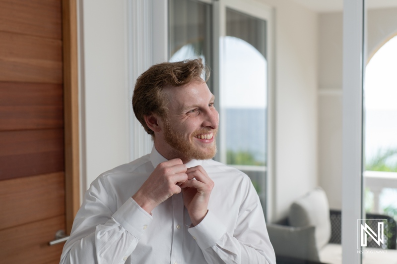 Groom preparing for wedding ceremony at Avila Beach Hotel in Curacao while adjusting his tie and smiling