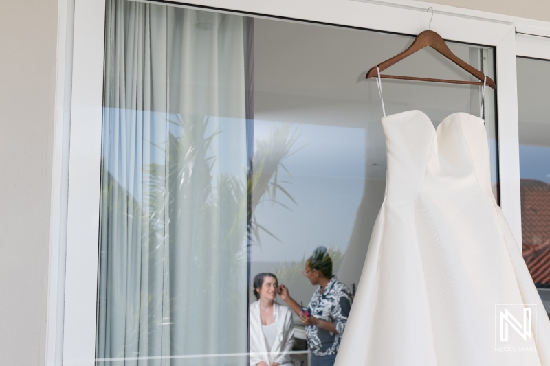 Bridal preparations at Avila Beach Hotel in Curacao featuring a wedding dress hanging by the window and a bride getting ready with assistance