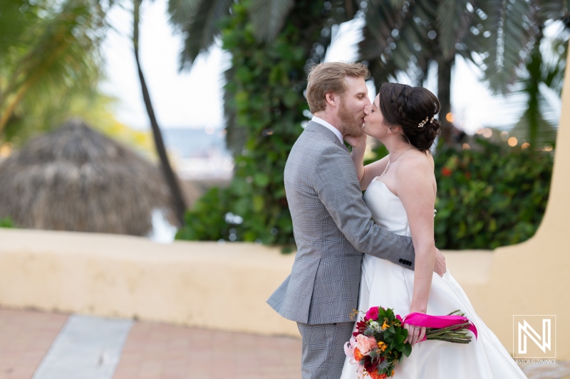 Couple shares a romantic kiss during their beach wedding at Avila Beach Hotel in Curacao under the palm trees
