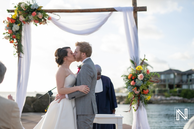 Couple shares a romantic kiss during their wedding ceremony at Avila Beach Hotel in Curacao, capturing the joy of love and celebration by the sea at sunset
