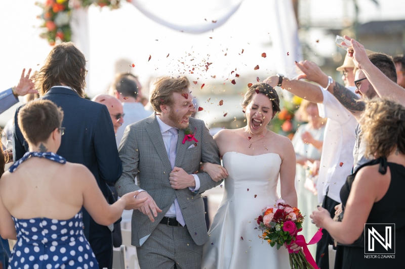 Couple celebrates joyful wedding at Avila Beach Hotel in Curacao with friends and family surrounded by vibrant floral decorations