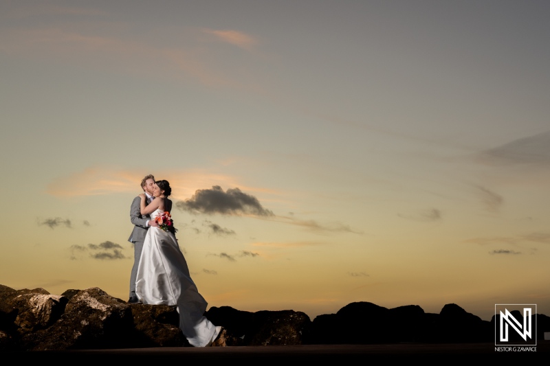 Couple embraces during sunset wedding ceremony at Avila Beach Hotel in Curacao, celebrating love against a stunning backdrop
