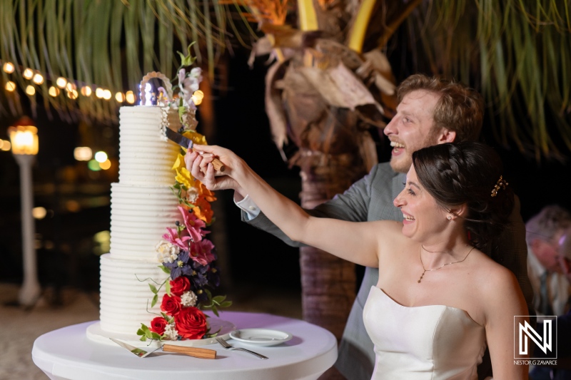 Couple joyfully cutting wedding cake at Avila Beach Hotel in Curacao under twinkling lights