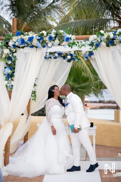 Couple shares a kiss during wedding ceremony at Avila Beach Hotel in Curacao under floral decorations
