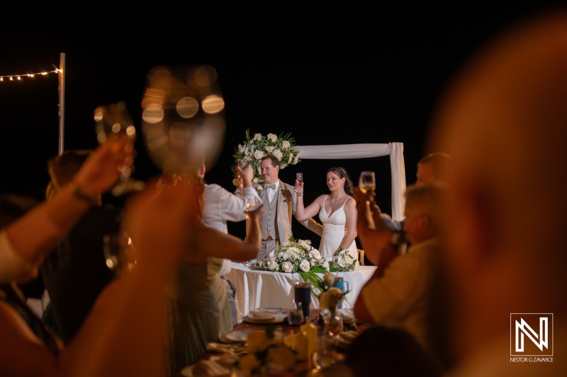 Couple celebrates wedding toast at sunset beach reception in Curacao at Sunscape Curacao Resort with guests raising glasses
