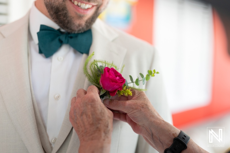 Couple prepares for wedding in Curacao with groom getting boutonniere attached by a friend or family member