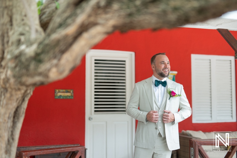 Wedding ceremony in Curacao at a bright red venue with a groom in a suit waiting for his bride to arrive