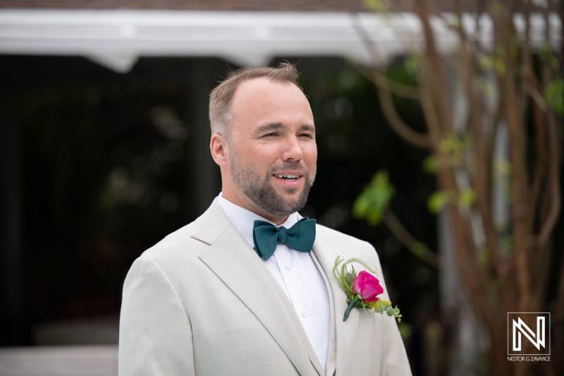 Wedding ceremony in Curacao features a man in formal wear standing outdoors with smiling expression