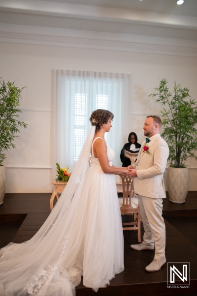 Couple exchanges vows during wedding ceremony in Curacao with guests present and tropical plants in the background