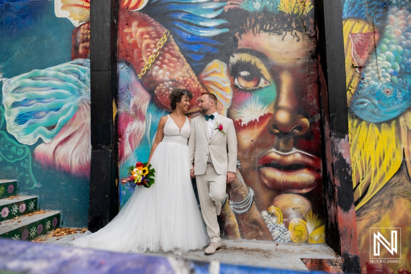 Couple celebrates wedding in Curacao with colorful mural in background during vibrant outdoor ceremony