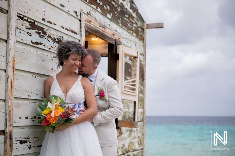 Couple enjoys a wedding moment by the beach in Curacao with colorful flowers and ocean background