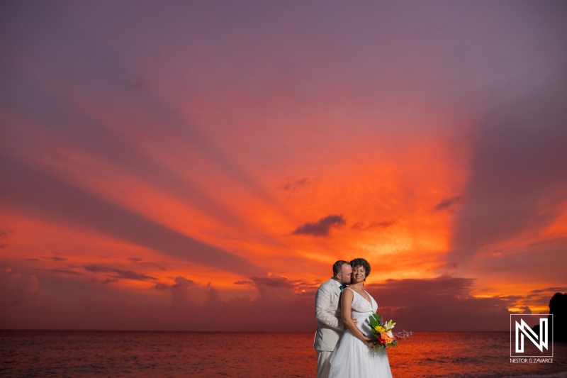 Couple enjoys sunset during wedding ceremony in Curacao on the beach with colorful sky and ocean waves in the background