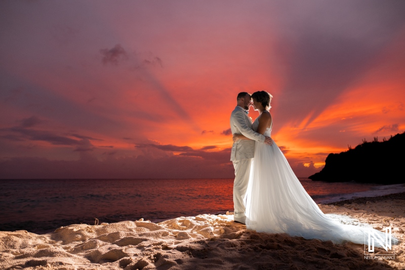 Couples stand on the beach in Curacao at sunset during their wedding ceremony while waves wash ashore