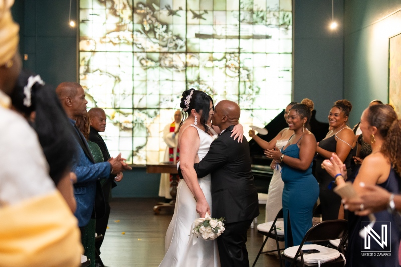 Couple shares a joyful kiss during their wedding ceremony at the Curaçao Museum, surrounded by friends and family celebrating the special occasion