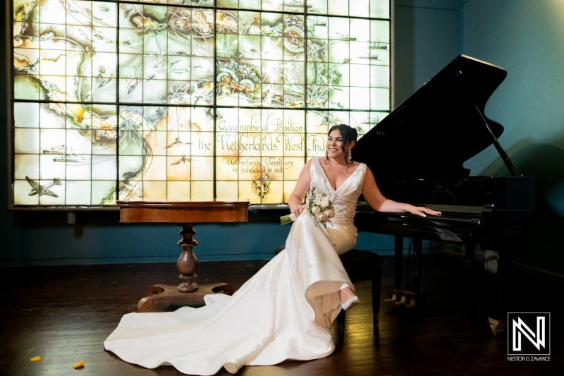 Beautiful bride seated at piano in Curaçao Museum during wedding ceremony under colorful stained glass window