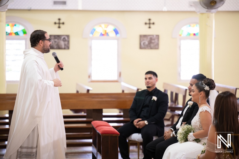 Wedding ceremony takes place in Curacao with guests seated and a priest speaking to the couple