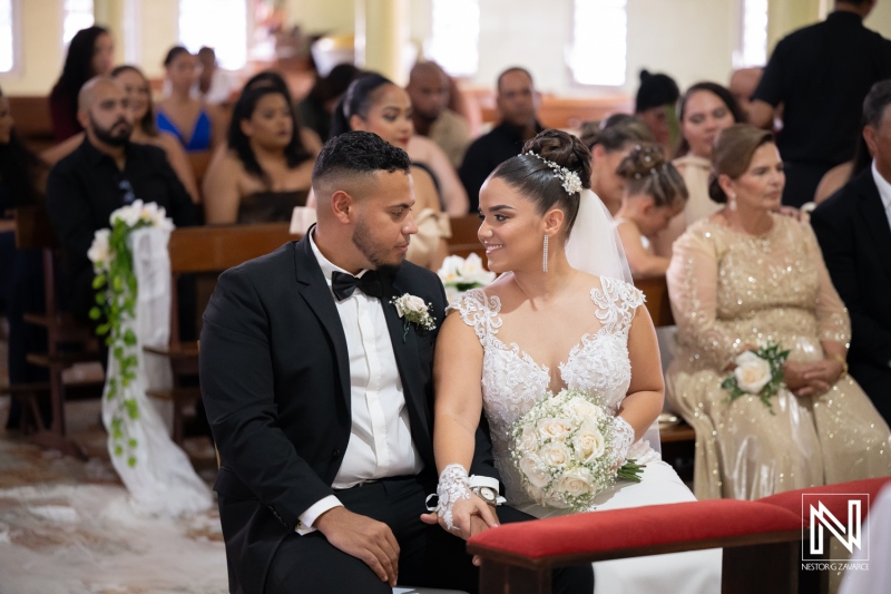 Couple sits together during wedding ceremony in Curacao, surrounded by friends and family in a church setting