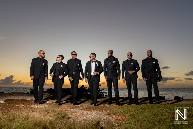 Groom and groomsmen enjoy sunset at wedding in Curacao with ocean views and relaxed poses
