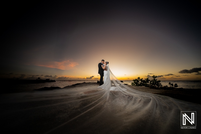 Couple enjoys wedding ceremony in Curacao at sunset with the ocean in the background and a long flowing veil