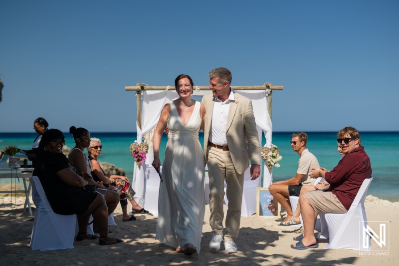 Couple walks hand in hand after wedding ceremony at Daaibooi Beach in Curacao under bright blue sky
